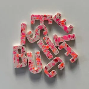 Bunte Buchstabenmagneten in Terrazzo-Optik auf grauem Hintergrund, Schriftzug "JUST BUST", kreative Workshops bei Elise Studio.