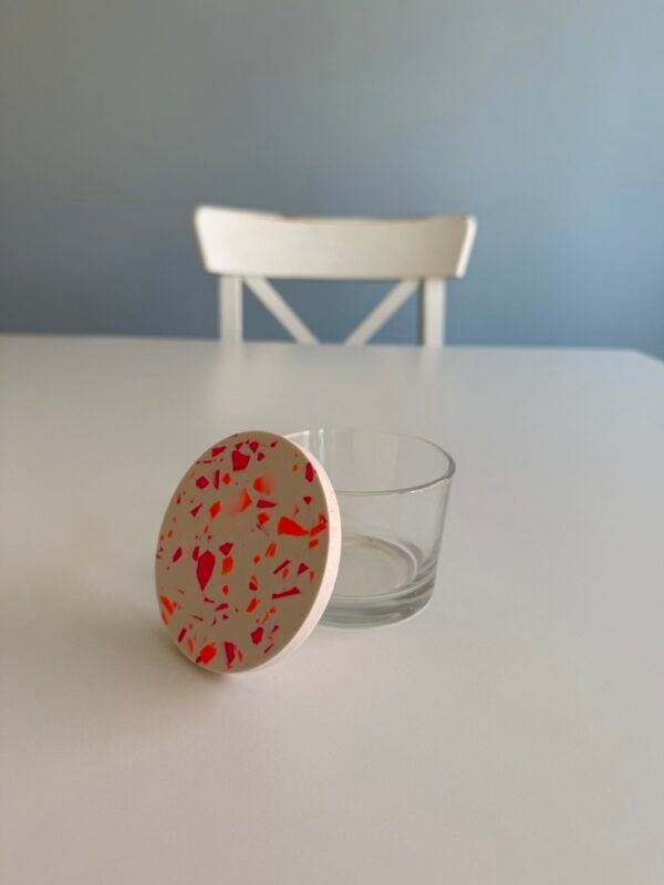 Terrazzo Glas mit weißem Deckel, pinken & orangen Chips im Studio.Elise Workshop, auf weißem Tisch mit Stuhl im Hintergrund.