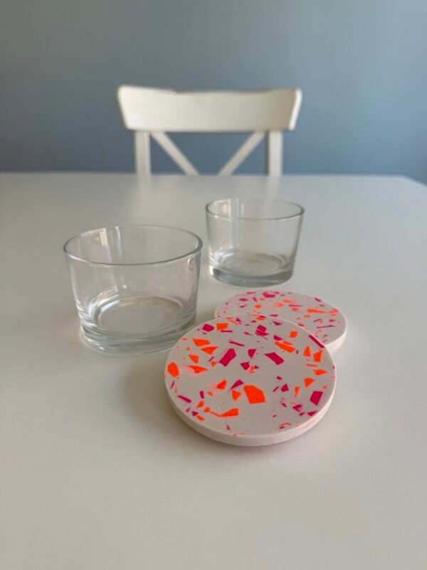 Terrazzo-Workshop: Zwei Gläser mit weißen Terrazzodeckeln, pinken & orangen Chips im Studio.Elise von Maike auf weißem Tisch.