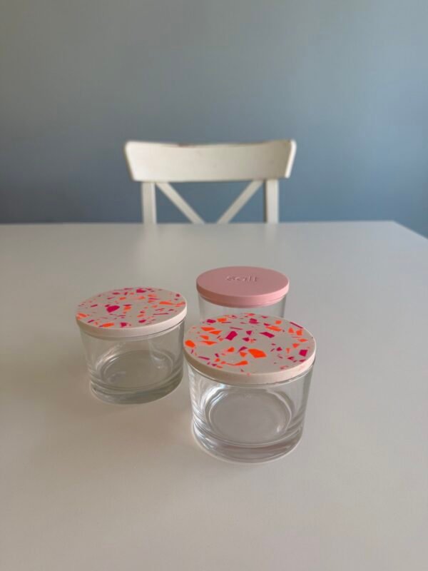 Terrazzo-Workshop: Drei Gläser mit weißen Deckeln, pinken & orangen Chips auf Tisch im Studio.Elise von Maike, Hintergrund Stuhl.