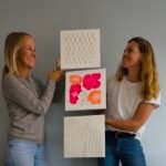 Maike und Teilnehmerin halten Terrazzo-Kunst aus Workshop im Studio Elise, mit Kreisen, Pink und Linien vor grauer Wand.