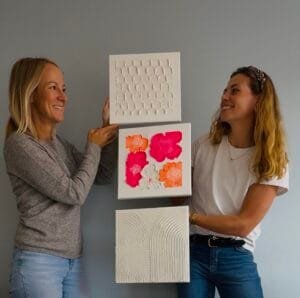 Maike und Teilnehmerin halten Terrazzo-Kunst aus Workshop im Studio Elise, mit Kreisen, Pink und Linien vor grauer Wand.