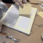 Maike gestaltet im Studio.Elise ein Terrazzo-Kunstwerk mit Spachtelmasse, umgeben von Farben, Pinseln und Workshop-Material.