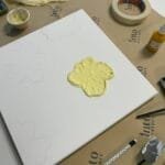 Terrazzo & Makramee Workshop bei Maike im Studio.Elise: Leinwand mit Blumenmotiv, Malzubehör und gelber Farbe auf Tisch.