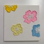 Strukturierte Kunstleinwand mit vier bunten Blumen auf weißem Hintergrund – Workshop im Studio.Elise für Makramee, Terrazzo & DIY.