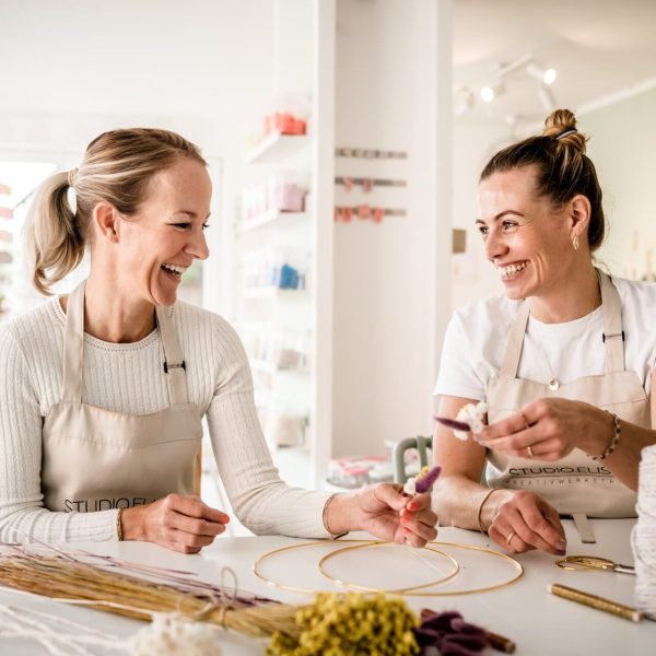 Zwei Frauen basteln beim Trockenblumen-Workshop im Studio: Elise mit Drahtreifen, Blumen und Makramee-Material, helle Atmosphäre.
